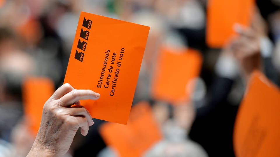 Eine Hand hält an der Versammlung der CVP eine orange Wahlkarte in die Höhe.