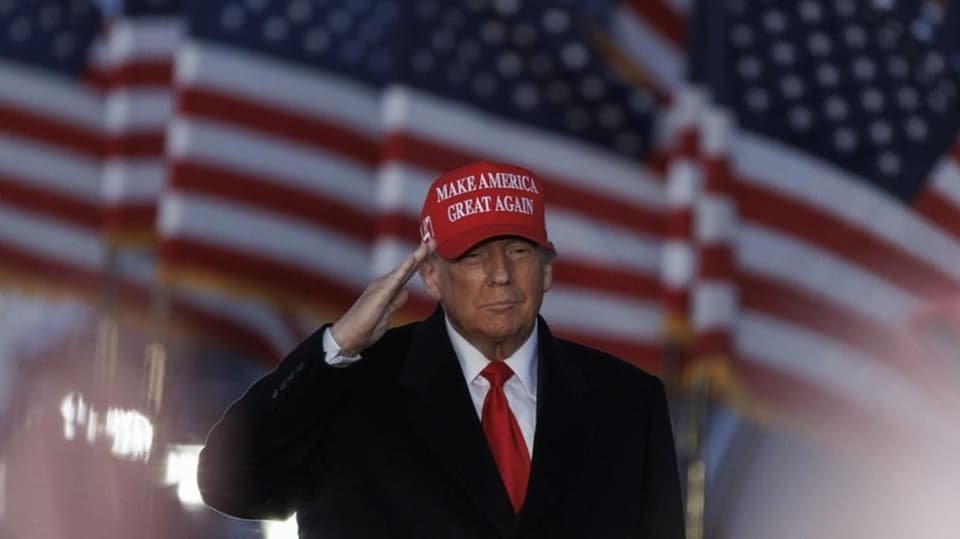 Ein alter blonder Mann salutiert vor US-Flaggen.