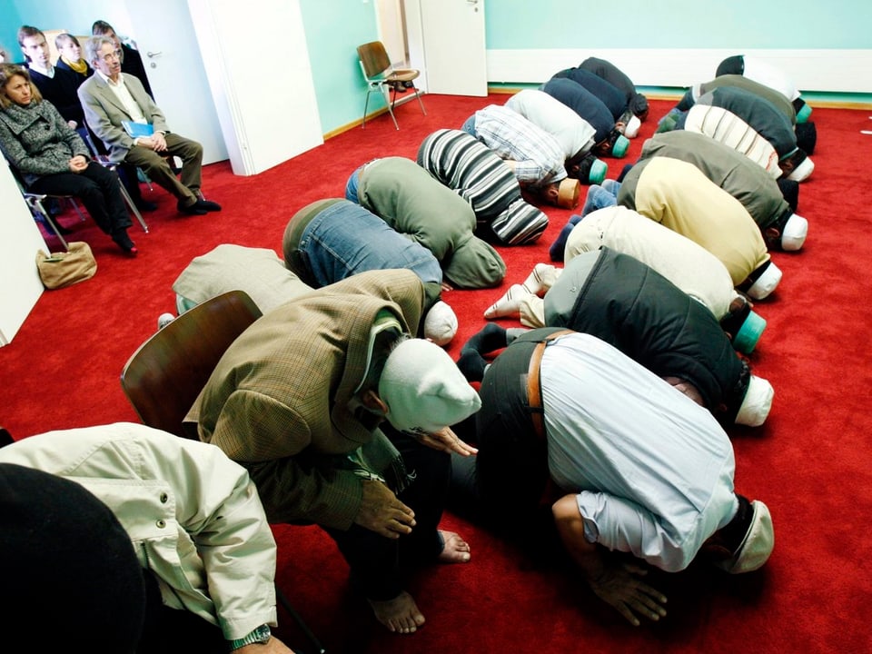 Menschen beten auf den Knien in einer Moschee. Symbolbild. 