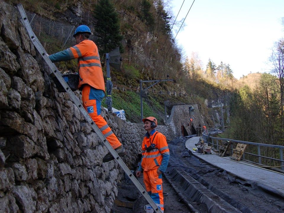 Zwei Arbeiter sanieren eine Natursteinmauer.