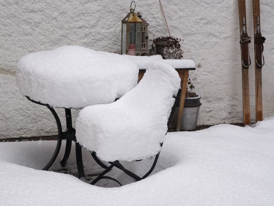 Gartenstuhl und Bank mit knapp 20 cm Schnee bedeckt.