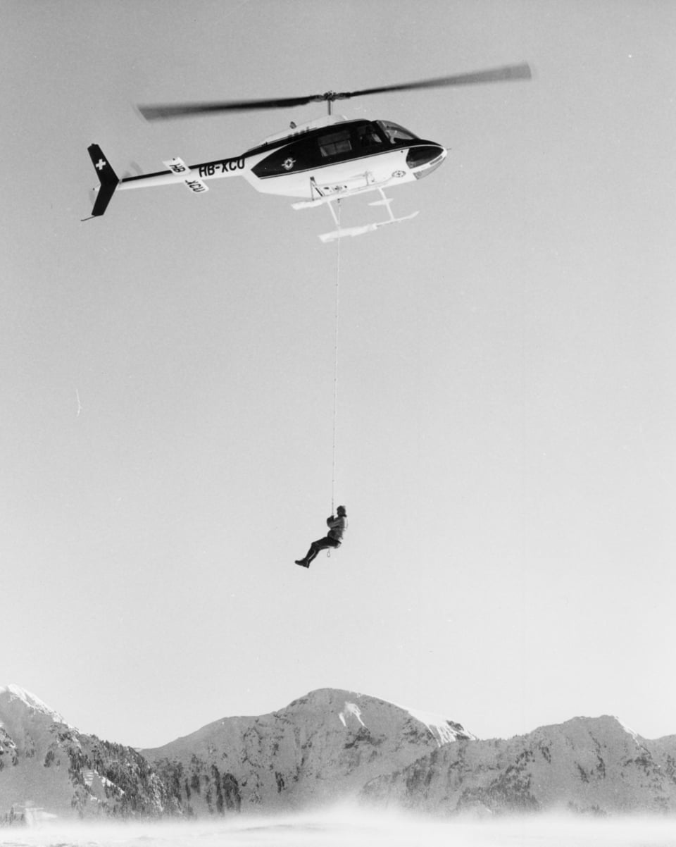 Ein Mensch hängt an einem Seil an einem Helikopter.