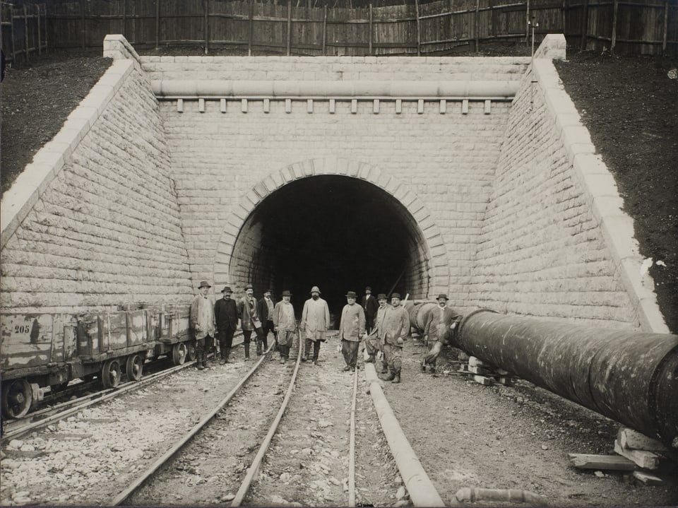 Schwarz-Weiss-Foto von einem Tunneleingang mit Arbeitern vordran. 