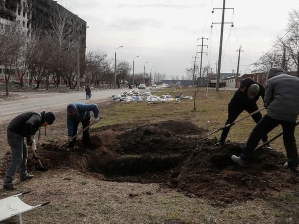 Männer heben in der belagerten Stadt Mariupol neben einer Strasse Gräber aus.