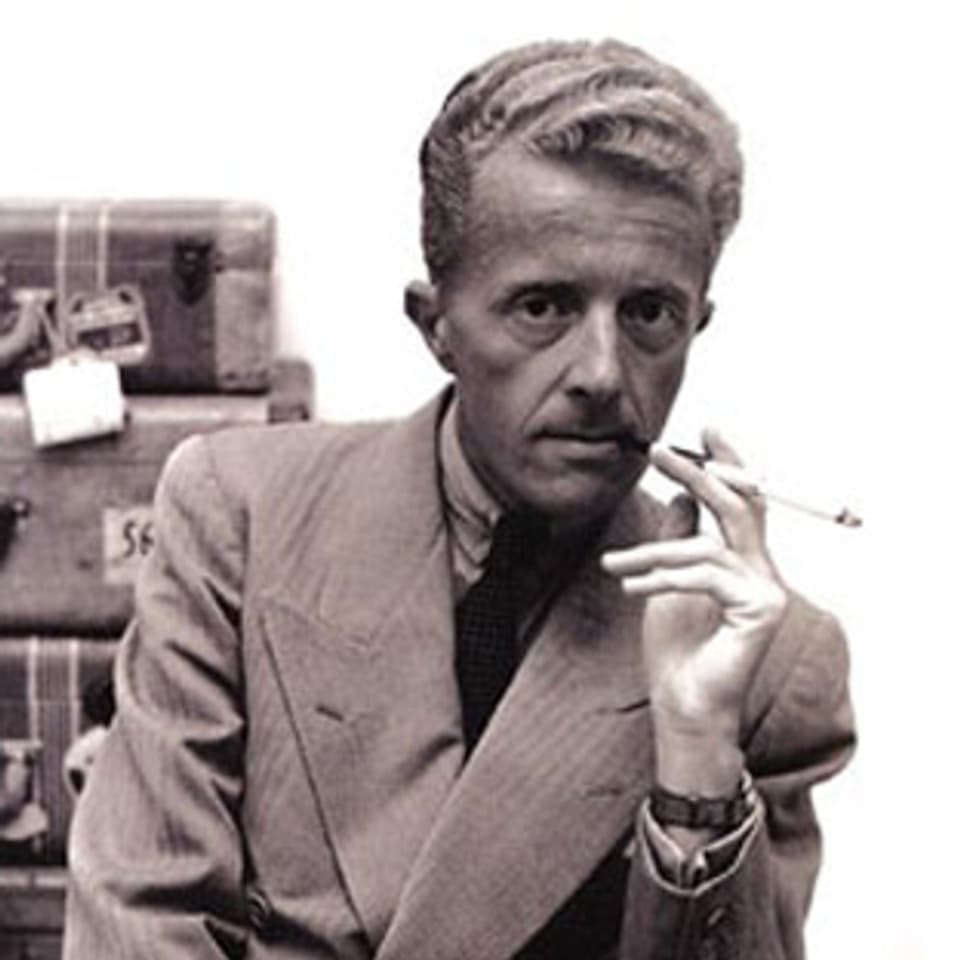 Schwarz-weiss Portrait des Schriftstellers Paul Bowles, der mit einer Zigarette in der Hand vor einem Stapel Koffern sitzt. 