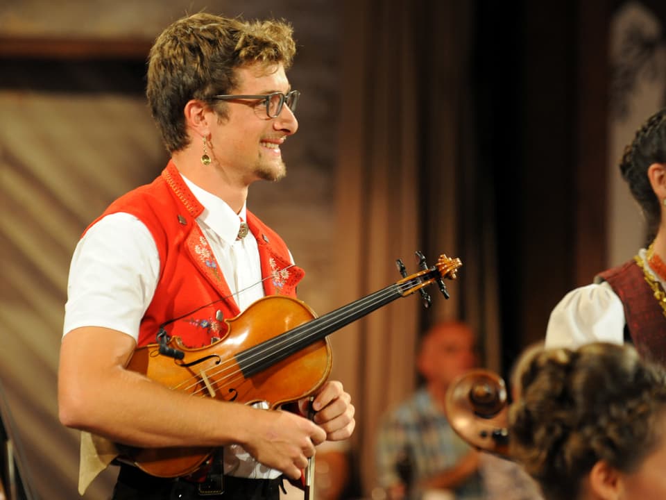 Geiger Damian Neff von Streichmusik Neff mit Geige in der Hand schaut lächelnd zur Seite.