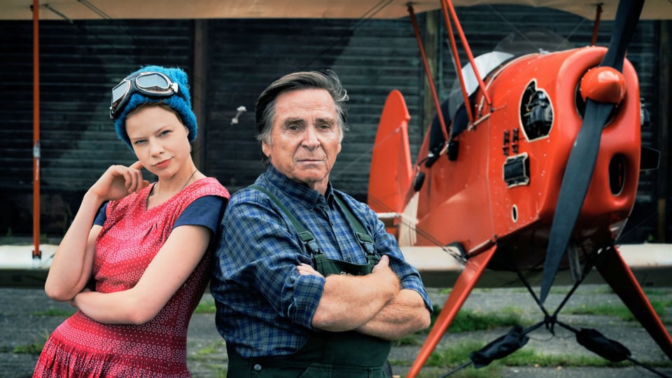 Ein junges Mädchen und ein Mann stehen vor einem alten Doppeldecker-Flugzeug.