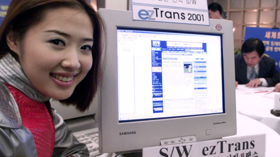 Eine Asiatin lächelt neben einem Bildschirm mit Übersetzungs-Software.