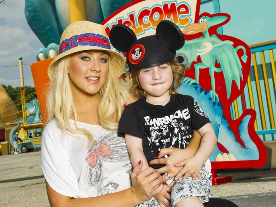 Blonde Frau mit Hut und einem Jungen mit Mickey-Mouse-Kappe auf dem Schoss.