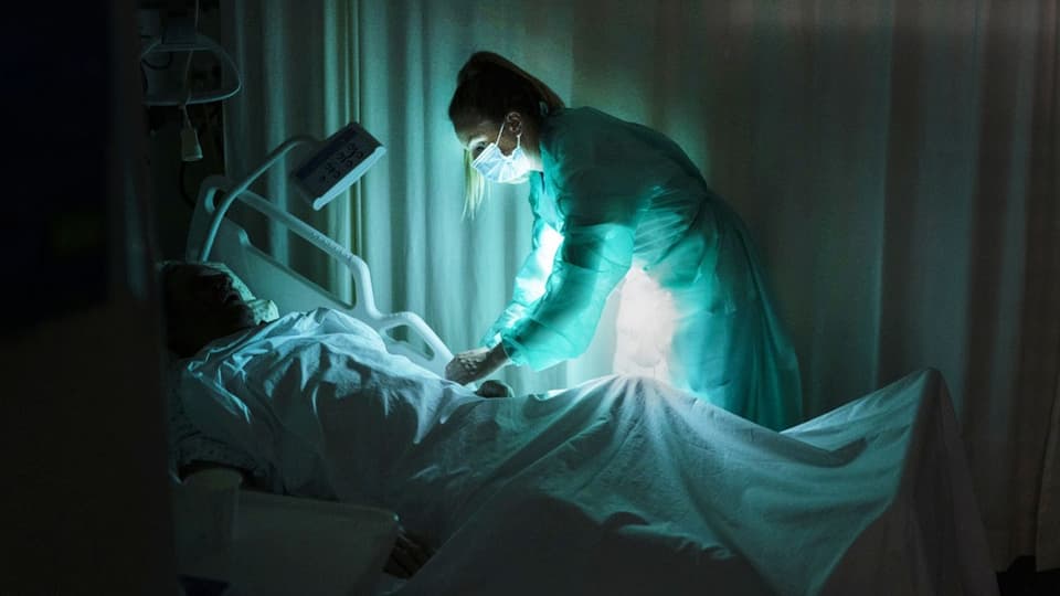 Bild einer Pflegekraft, die an einem Krankenbett beugt.