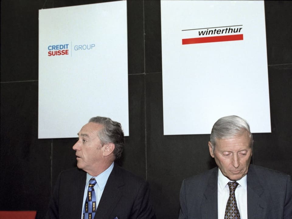 Zwei Männer sitzen auf Podium, mit Logos der Credit Suisse und der Winterthur Versicherung im Hintergrund