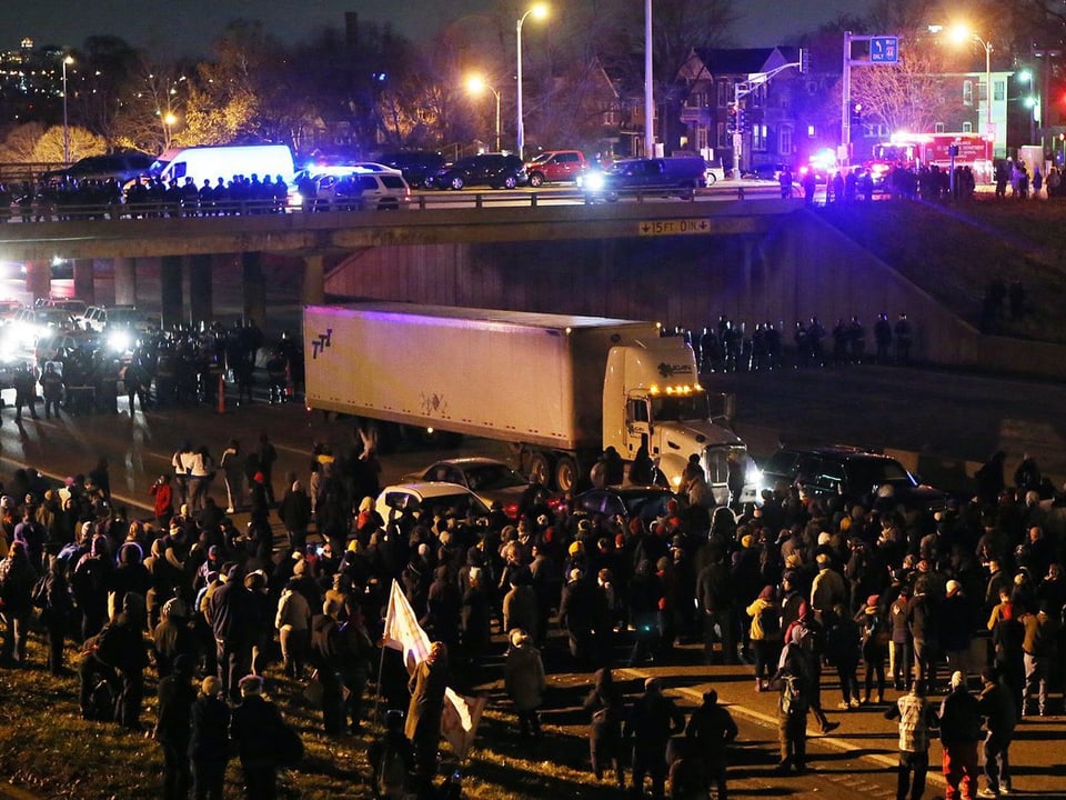 Demonstrierende blockieren eine Strasse, auf der sich der Verkehr staut