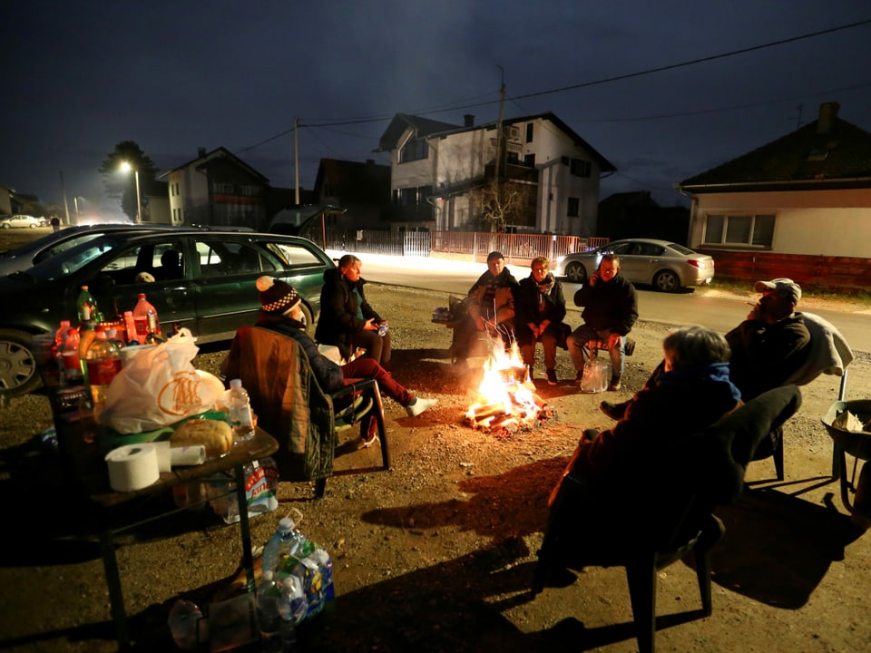 Menschen sitzen um ein Feuer im Freien.