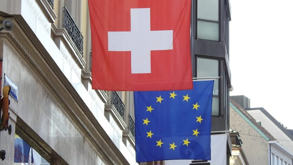 Schweizer und EU-Flagge hängen an einem Gebäude.