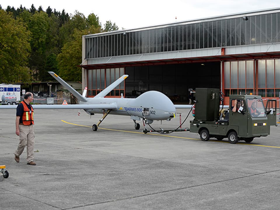 Die Drohne wird von einem kleinen Fahrzeug neben einem Hangar gezogen.
