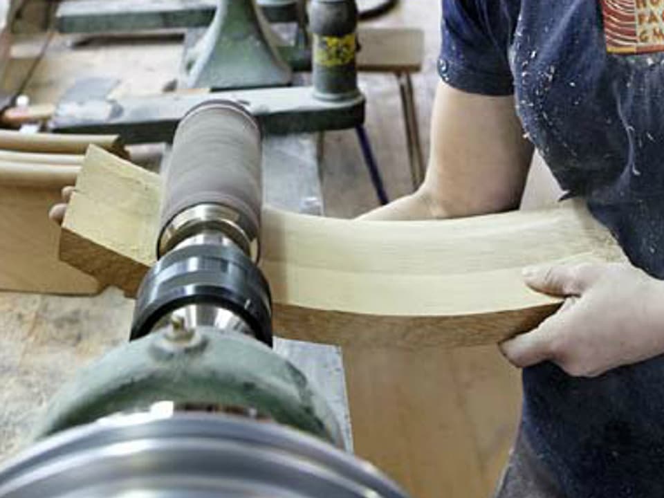 Ein bekrümmtes Holzstück wird an die Schleifmaschine gedrückt.
