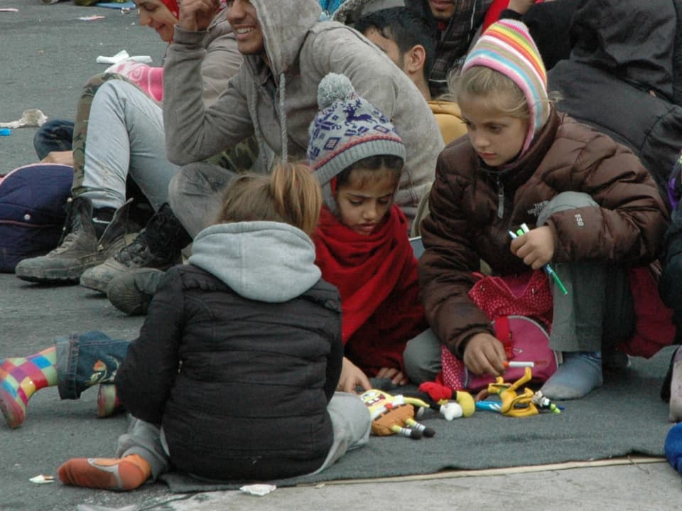 Dre  Kinder sitzen auf dem Boden und spielen mit Puppen.