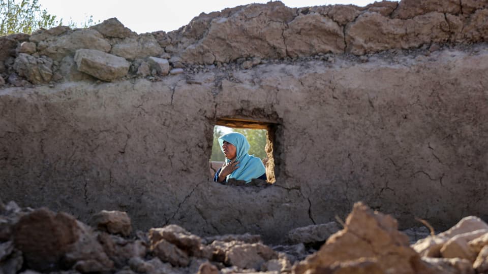 Blick durch kleines Fenster eines zerstörten Lehmhauses auf weinende Frau