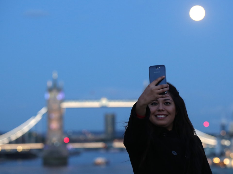 Eine Frau nimmt sich mit dem Mond vor der Tower Bridge auf