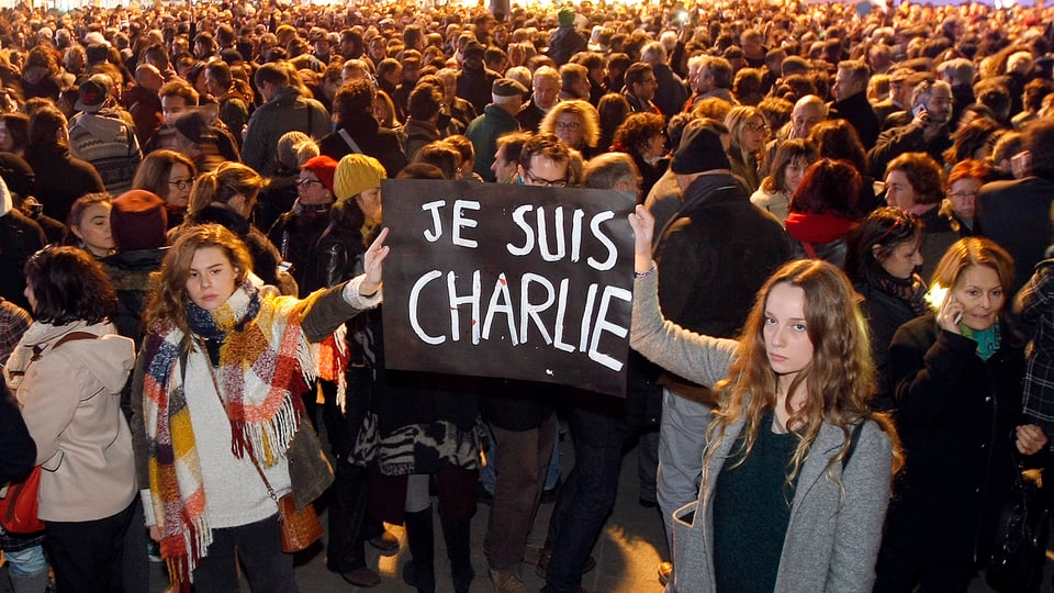Zwei junge Frauen halten ein Plakat in die Höhe, auf dem Je suis Charlie geschrieben steht.