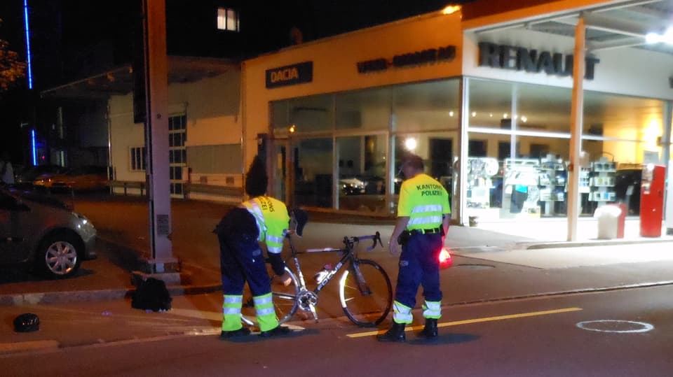 Zwei Kantonspolizisten untersuchen ein Fahrrad, ein Velohelm liegt daneben am Boden.