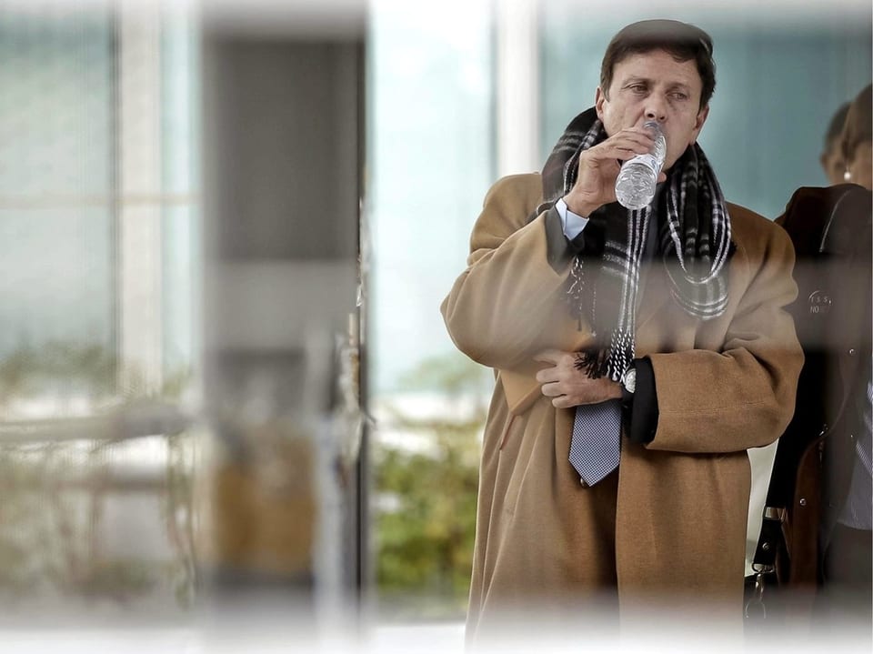 Man in coat drinks water from water bottle.