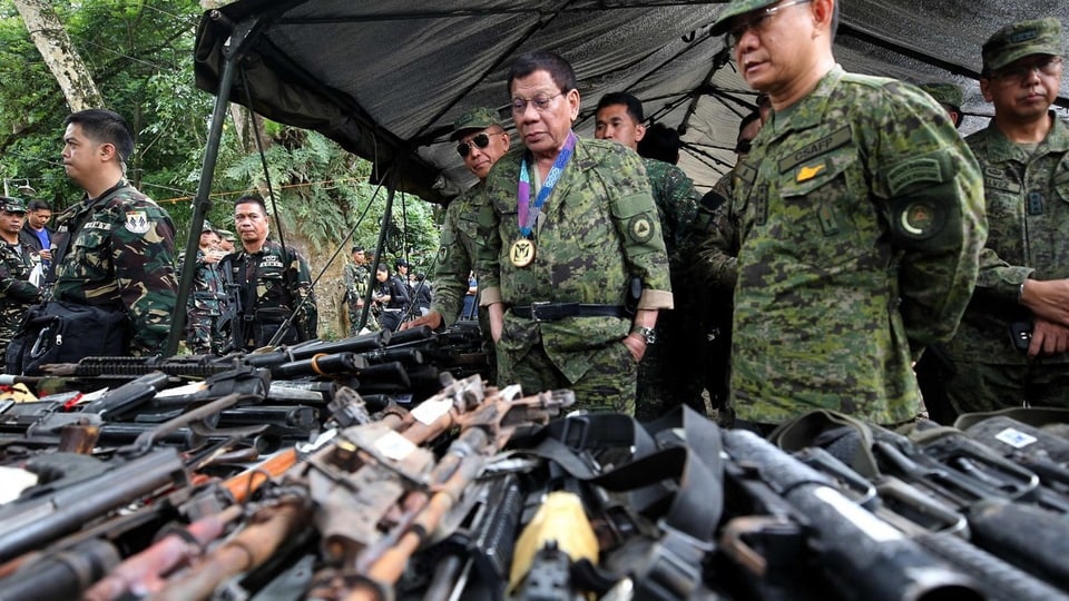 Mehrere Männer in Uniform schauen sich Waffen auf Tischen an.