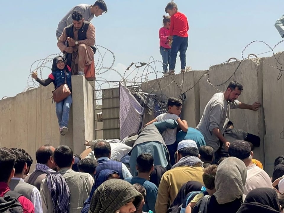 Menschen überqueren die Mauer des Flughafens von Kabul.