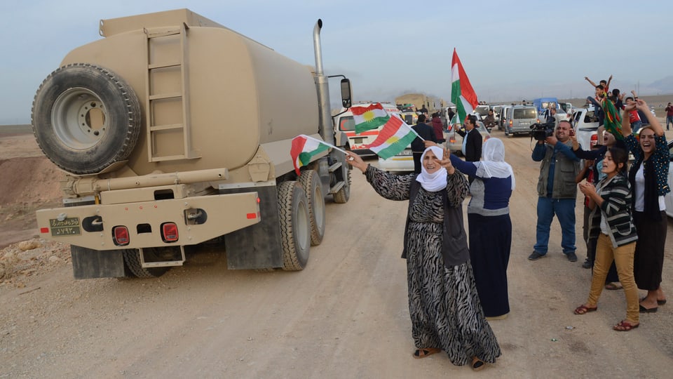 Kurden heissen die Lastwagenkolonne der Peschmerga willkommen und schwengen Fähnchen.