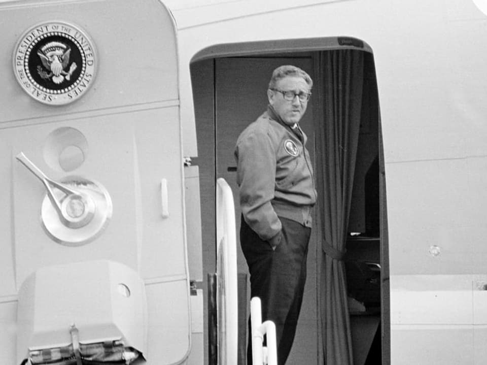 Henry Kissinger steht mit den Händen in den Hosentaschen im Eingang der Air Force One, dem Flugzeug des US-Präsidenten.