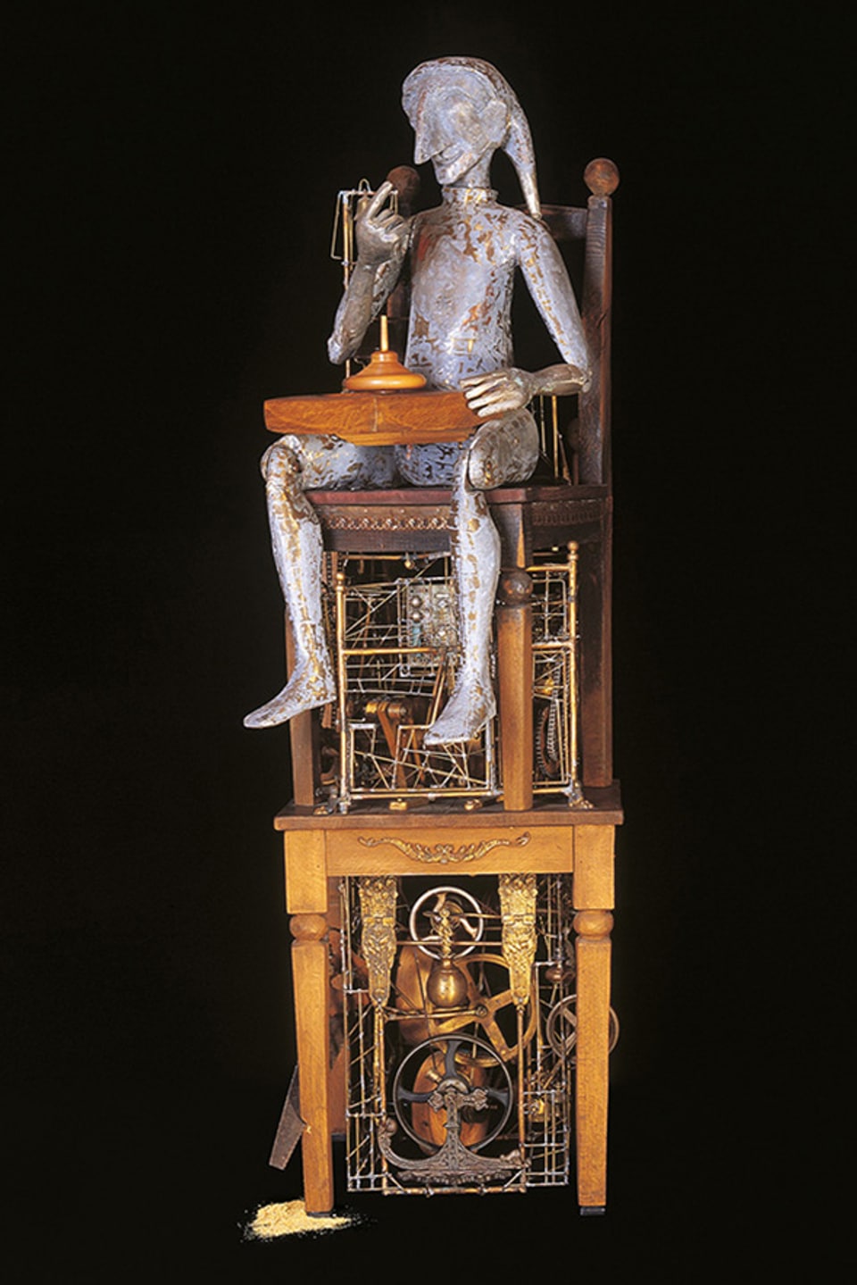 Skulptur einer Figur, die auf zwei Stühlen sitzt. 