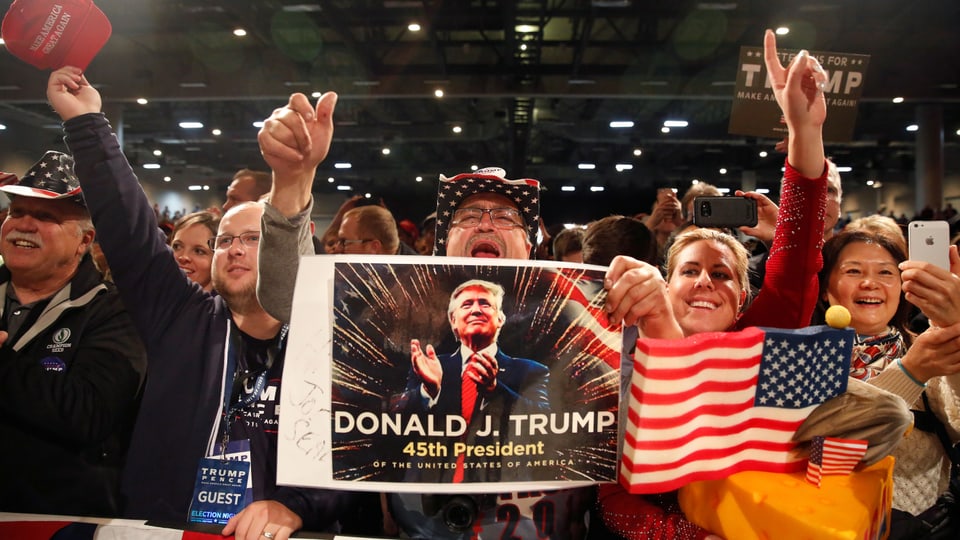 Jubelnde Menschen mit Amerkia-Flagge und Poster von Donald Trump.