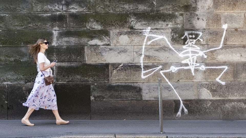 Eine Frau läuft an einer Mauer mit Graffiti vorbei.