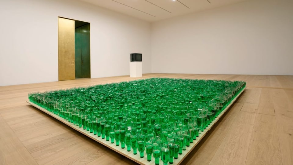 Raum mit grossen Fläche voll von halbierten, grünen Flaschen, die umgekehrt in einer Holzplatte stecken.