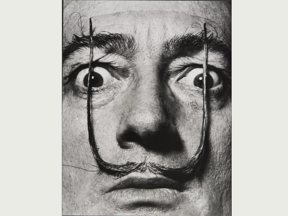 Porträt von Salvador Dali, den Schnauz gerade hoch gezogen vor die Augen, die Augen weit geöffnet.