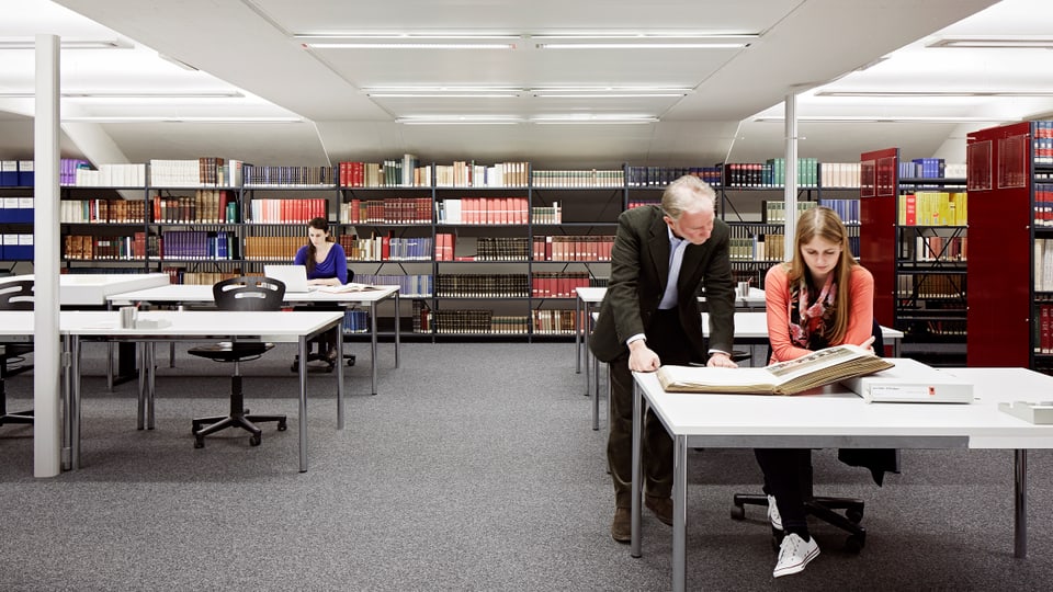 Bibliothek mit zahlreichen Tischen, an denen Menschen arbeiten.