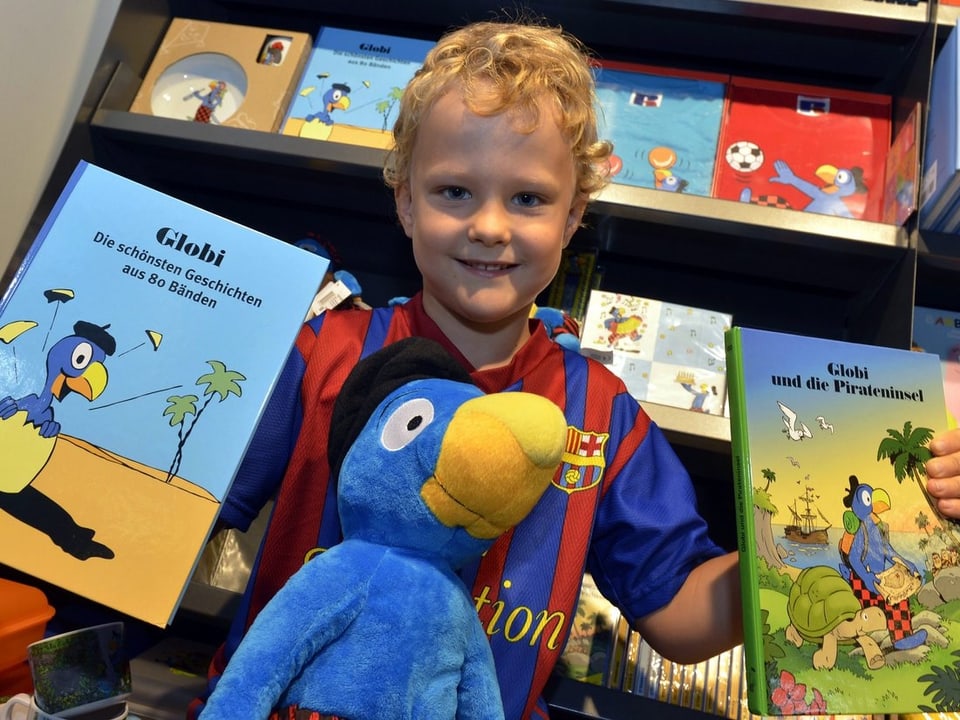 Kind mit Plüschglobi und zwei Globi-Büchern vor Bücherregal