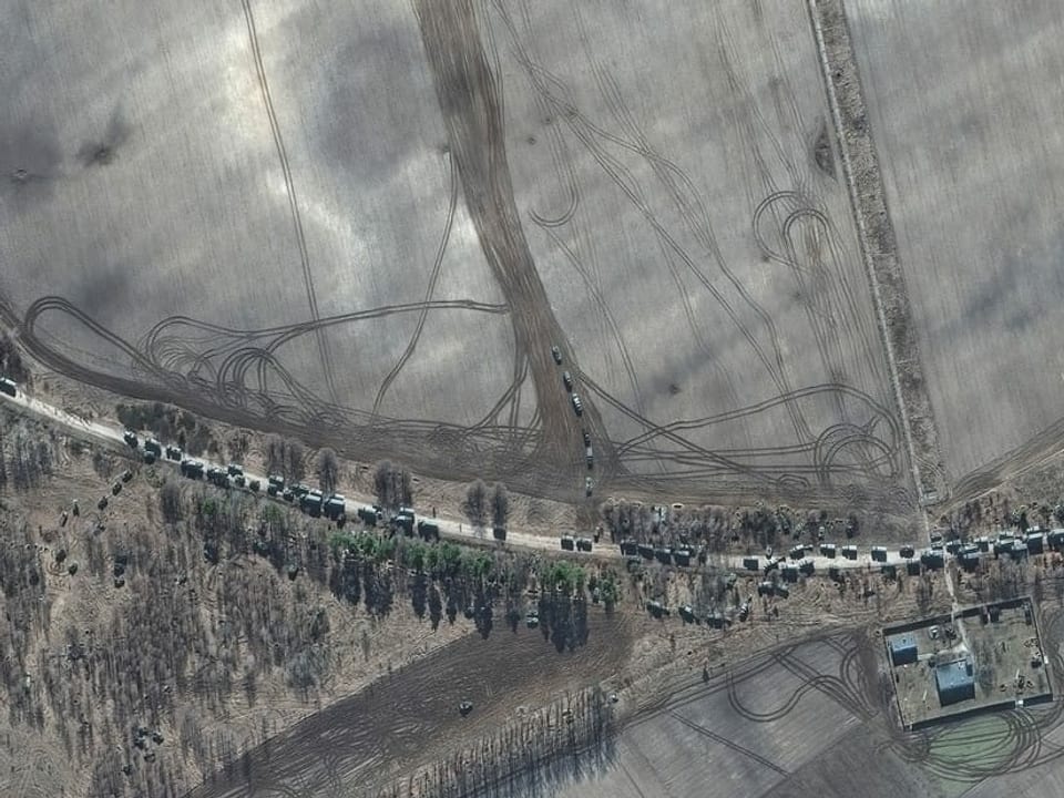 Vogelperspektive: Eine Landstrasse wird von dutzenden Militärfahrzeugen verstopft.  