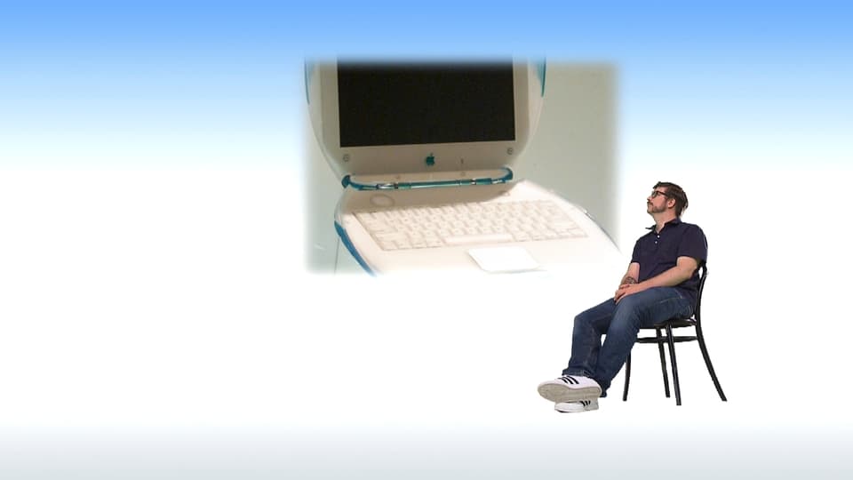 Guido Berger sitzt auf einem Stuhl und schaut ein Bild eines alten Computers an.