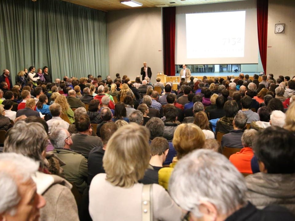 Ein Saal, gefüllt mit Menschen auf Stühlen.