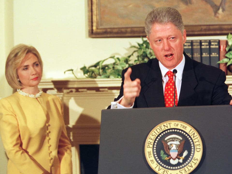 Bill Clinton an einem Rednerpult – Hillary Clinton steht dahinter.