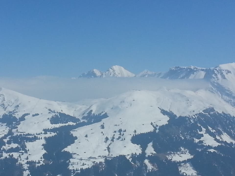 Blauer Himmel, verschneite Berge und hinter den ersten Bergen Hochnebel.