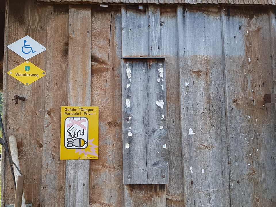 Stallwand aus Holz mit Wanderzeichen und Warnschild Blindgänger