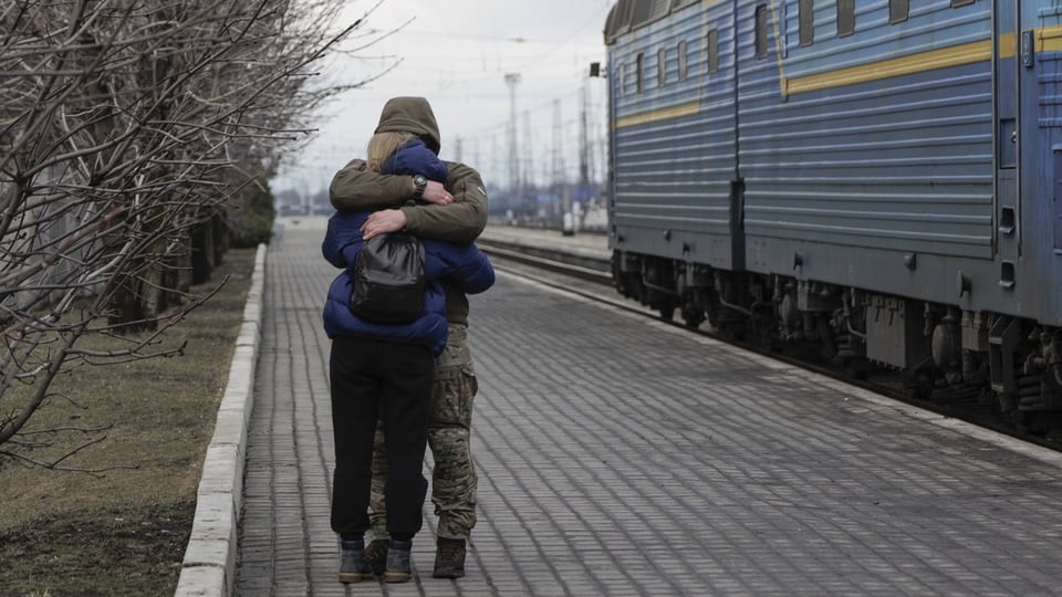 Eine Frau umarmt ihren Mann an einem Bahnhof. 