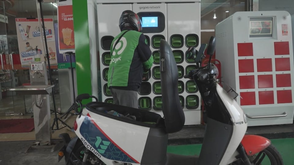 Pengemudi Gojek mengganti baterai pada e-motornya.