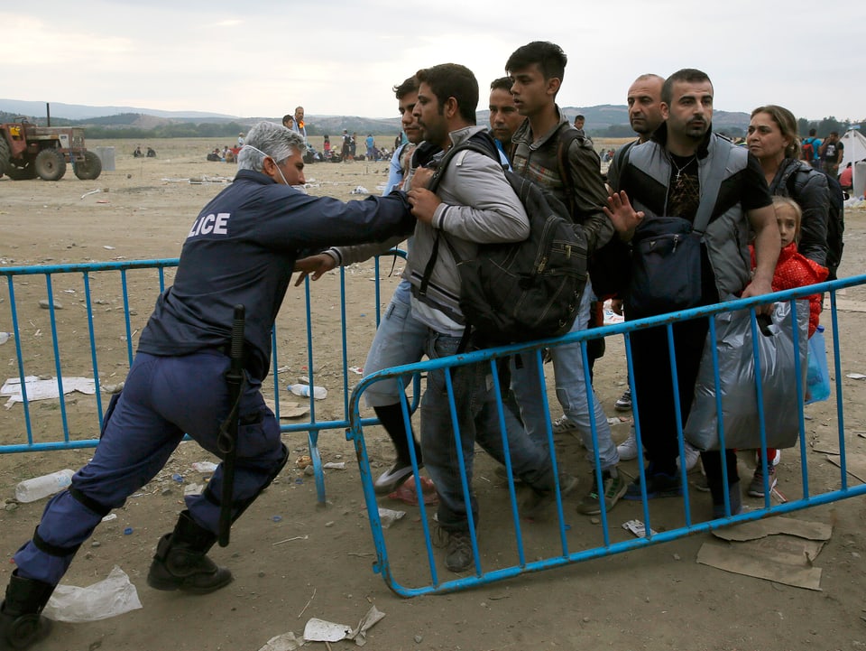 Ein griechischer Polizist stösst Flüchtlinge zurück hinter eine Barriere