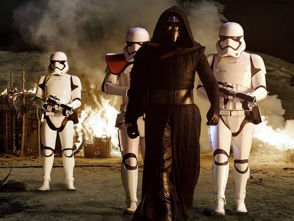 Film scene: Man in black suit with mask in front of white soldiers with helmets.