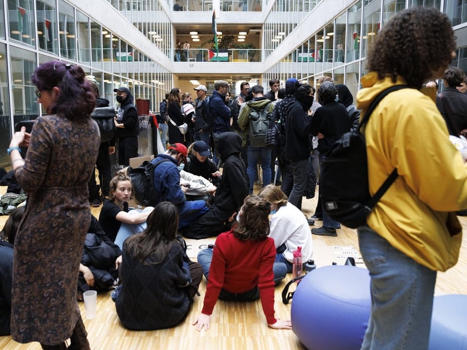 Menschen in einer belebten modernen Atrium-Lobby eines Gebäudes, einige sitzen auf dem Boden.