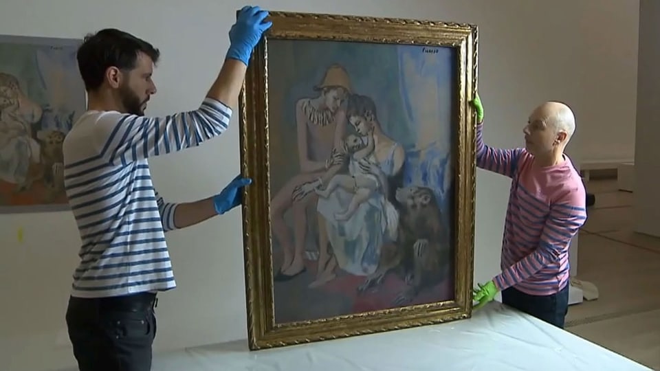 Zwei Männer mit Handschuhen halten ein Gemälde