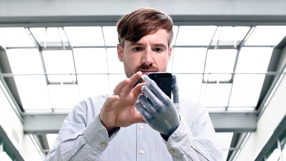 Bertolt Meyer hält ein Smartphone mit seiner Prothese und tippt mit der anderen Hand. 